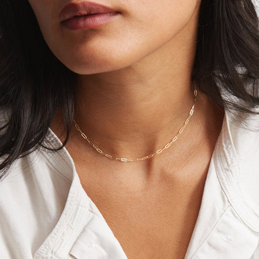 Model draagt een korte elliptische ketting van 14K goudkleurig titaniumstaal, minimalistische damessieraden