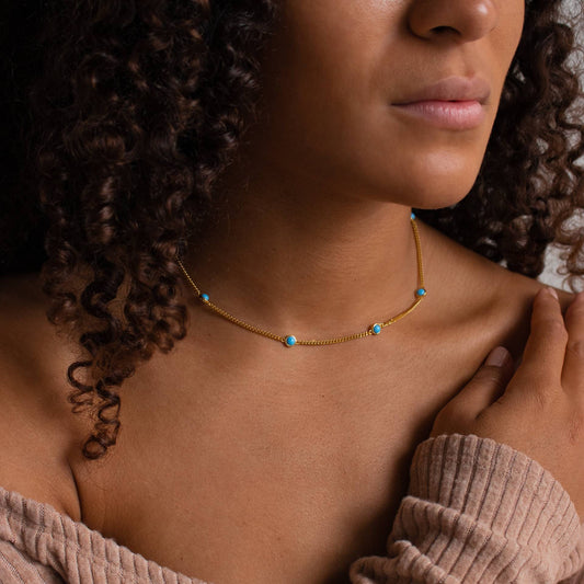 Model draagt een gouden titanium stalen ketting met turquoise franjes en zirkoon.