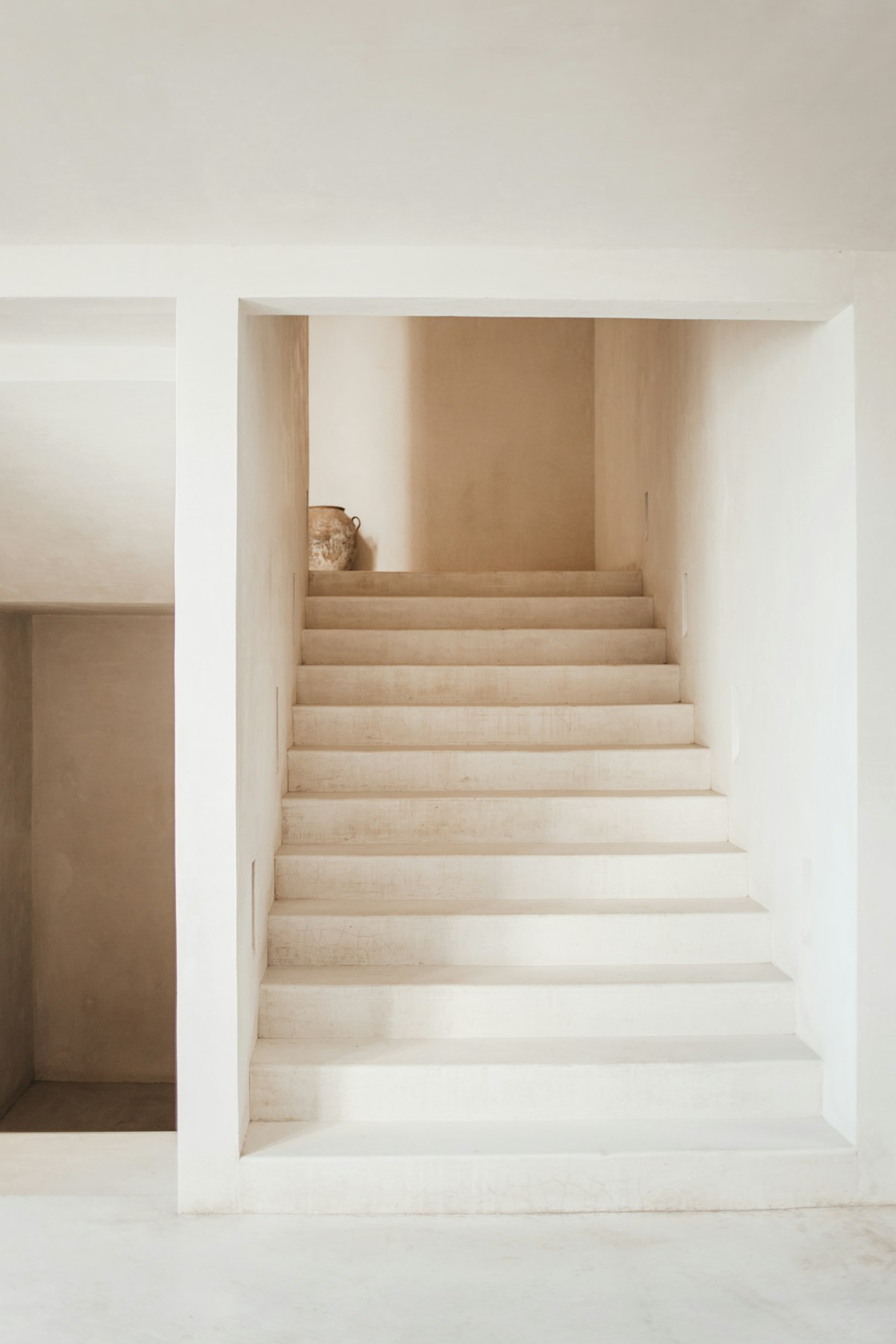 Minimal white staircase with a ceramic vase on the landing