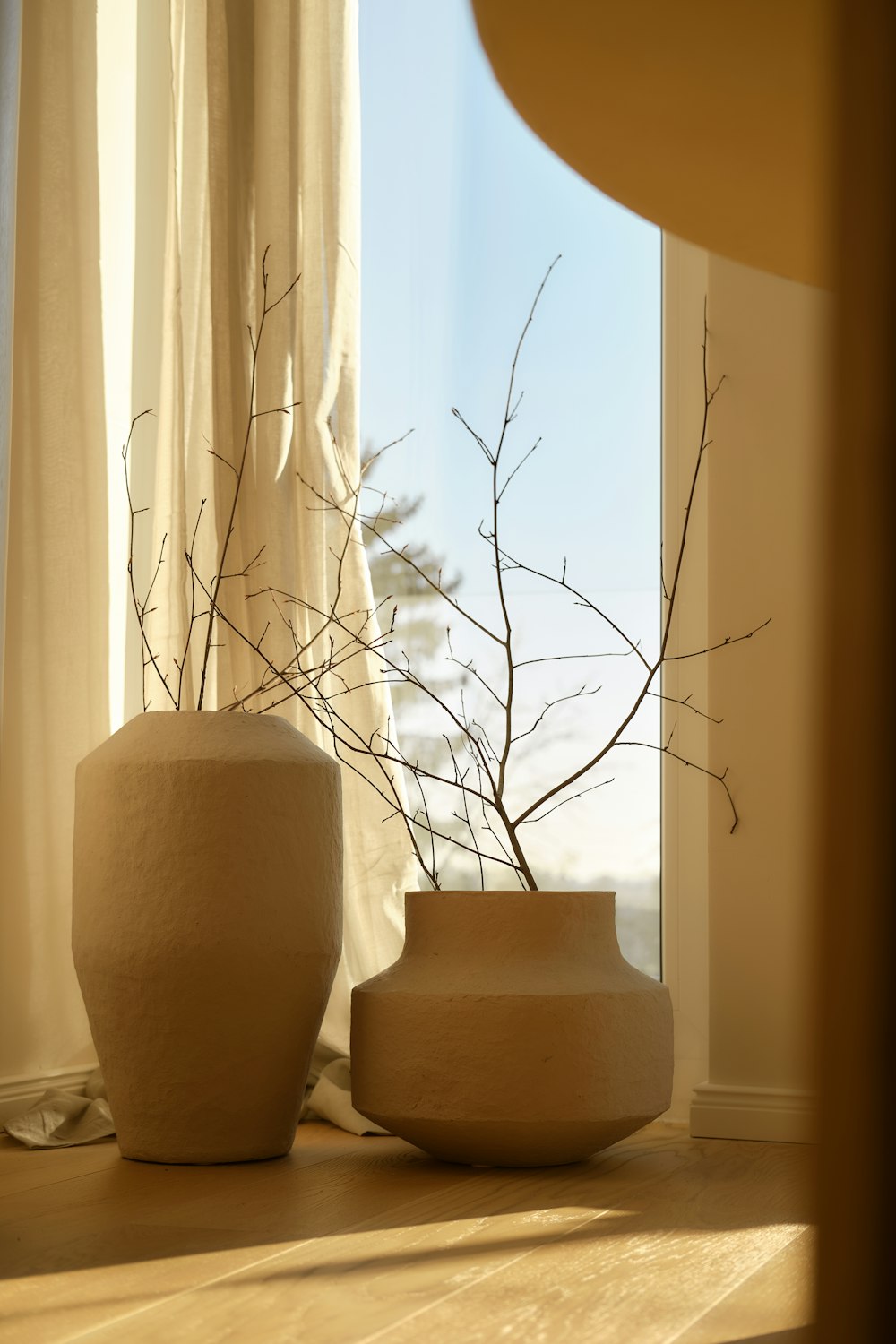 Two textured ceramic vases with dried branches beside a window